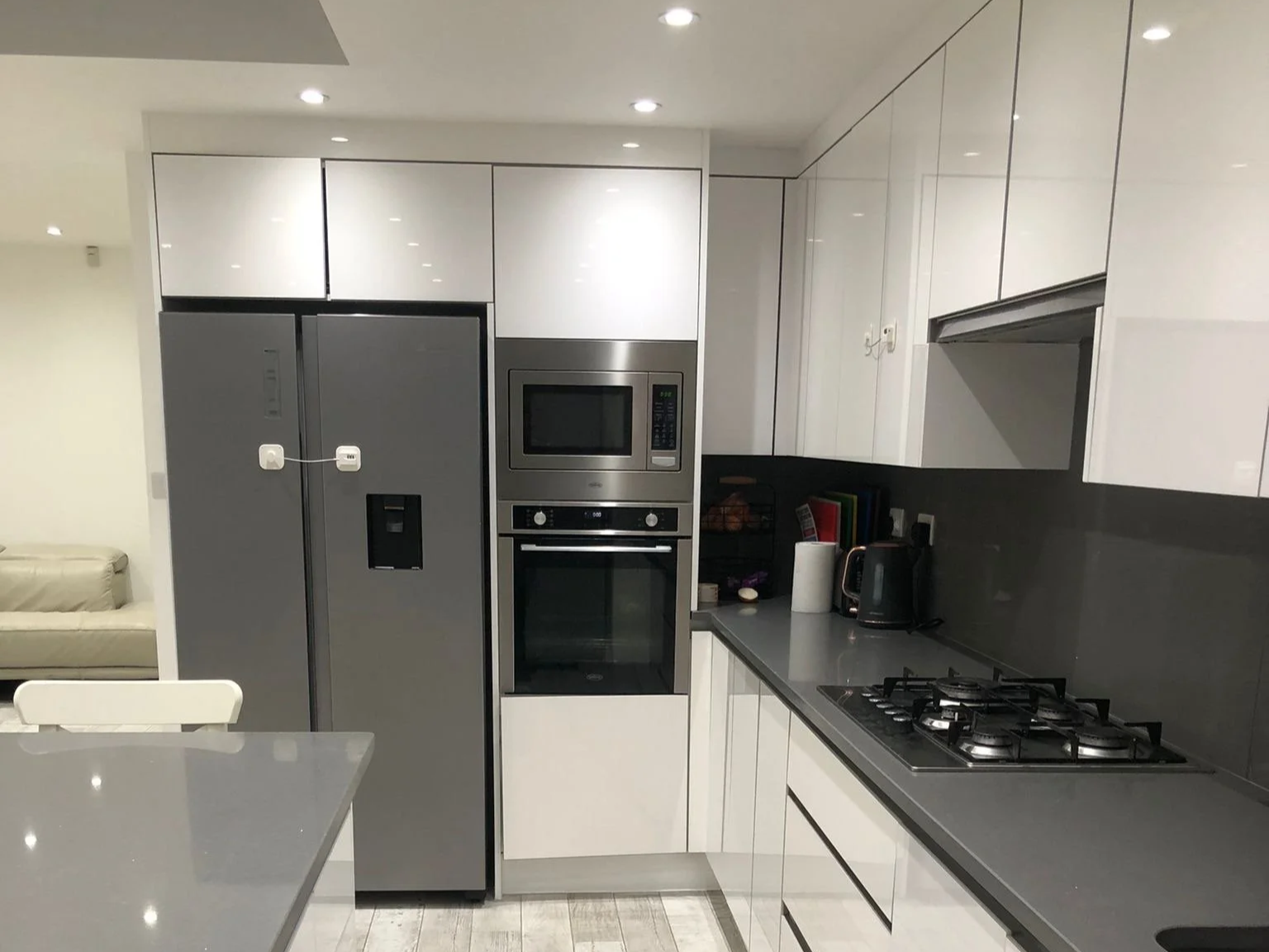 Modern bedroom with white walls, gray carpet, two windows with closed blinds, a bed with a cartoon animal print duvet, a small bedside lamp, and a black radiator.
