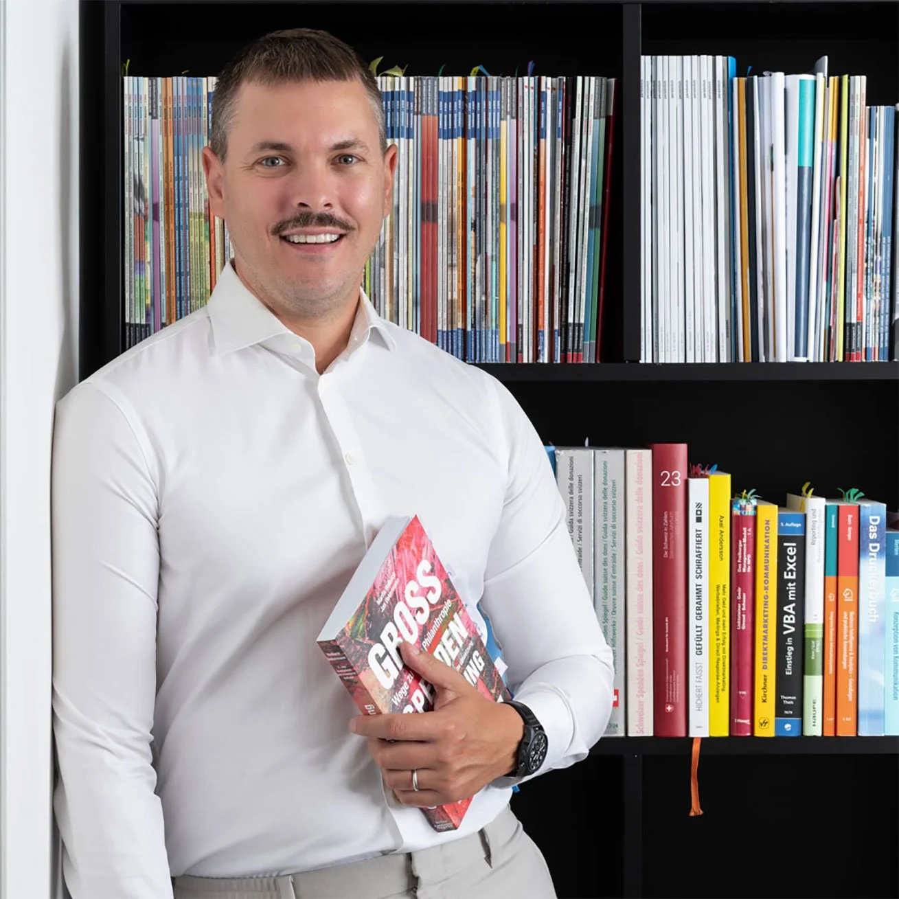 Brian Hemmi, Fundraising-Berater und Experte in einem weißen Hemd vor einem Bücherregal mit bunten Büchern rund um Fundraising