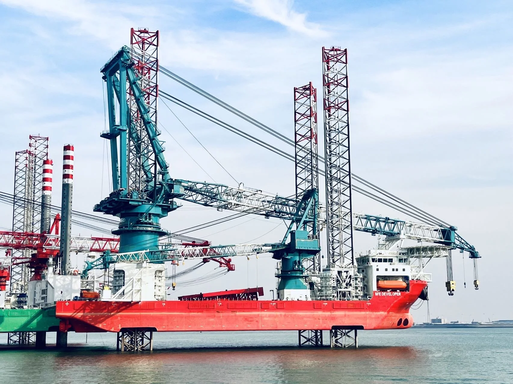An offshore oil platform with cranes and equipment surrounded by water under a partly cloudy sky.