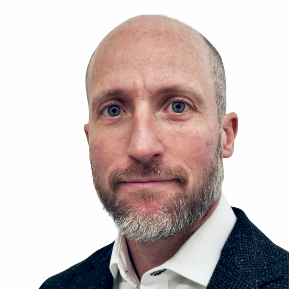 Portrait d'un homme avec une barbe, portant une chemise blanche et une veste noire, contre un fond blanc.