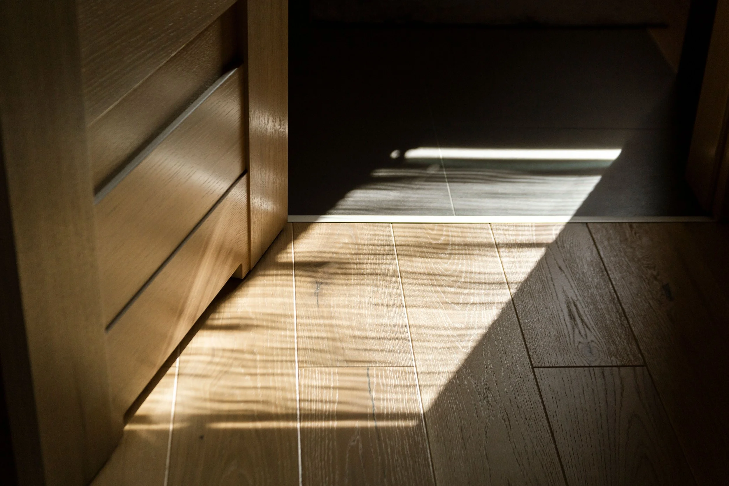 Rectangular sunlight and soft shadows falling across a warm wooden floor.