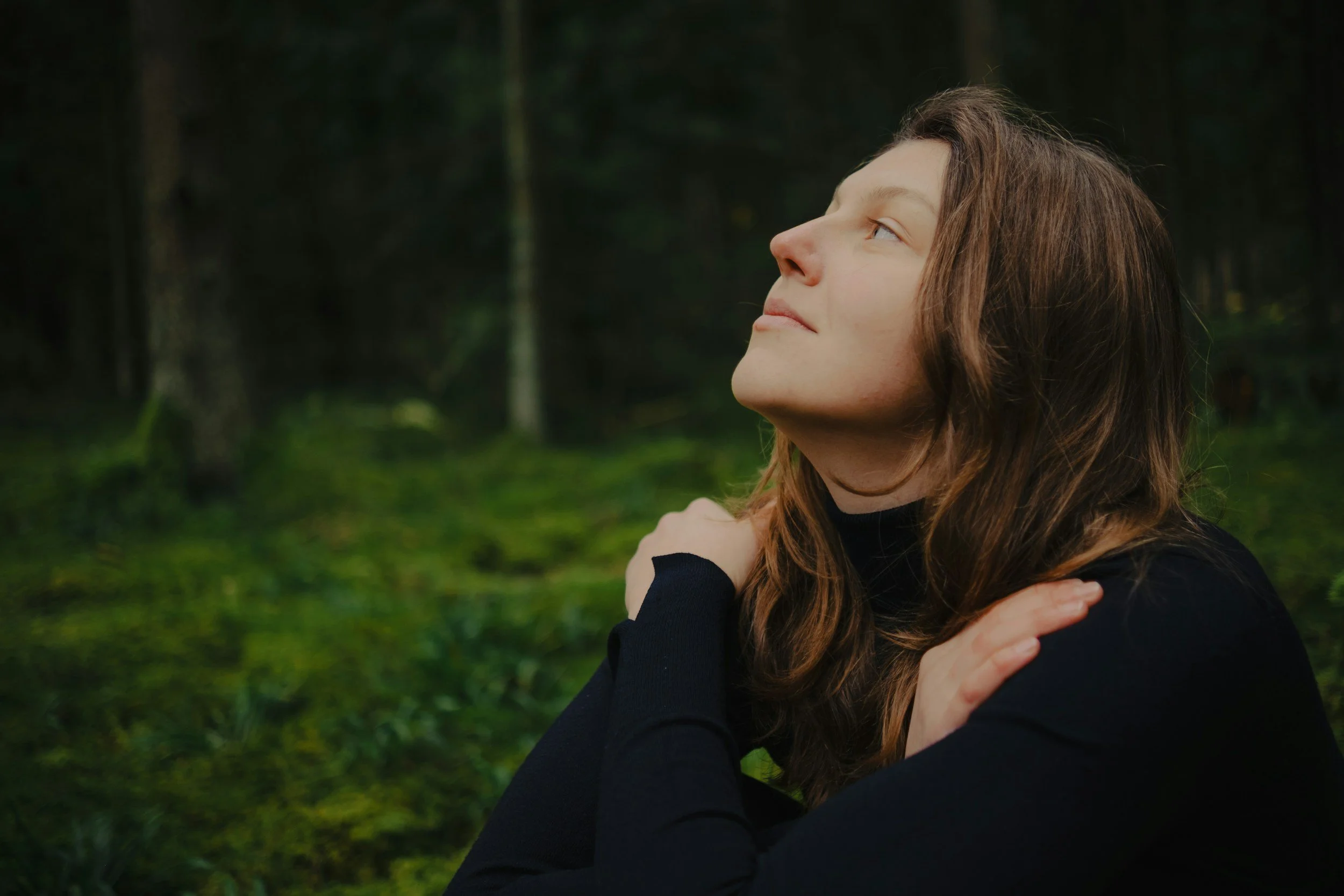 Woman sitting outdoors with her arms gently crossed over her shoulders.