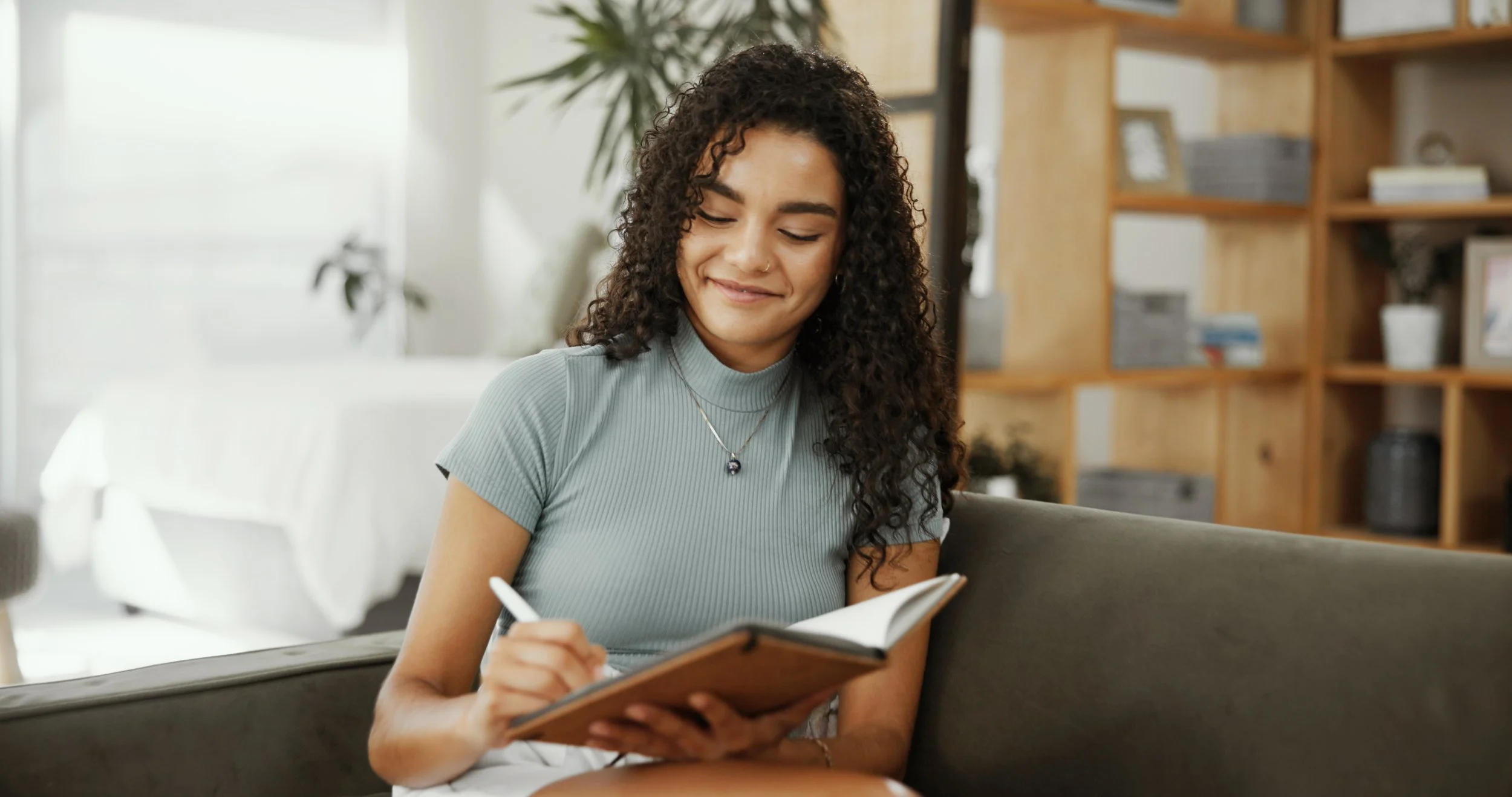 Woman sitting on a couch and writing in a journal.