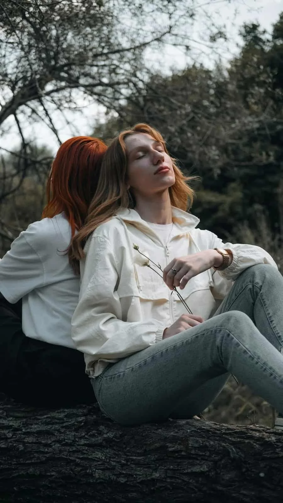 Two people sitting back-to-back outdoors, sharing closeness while one rests with her eyes closed.