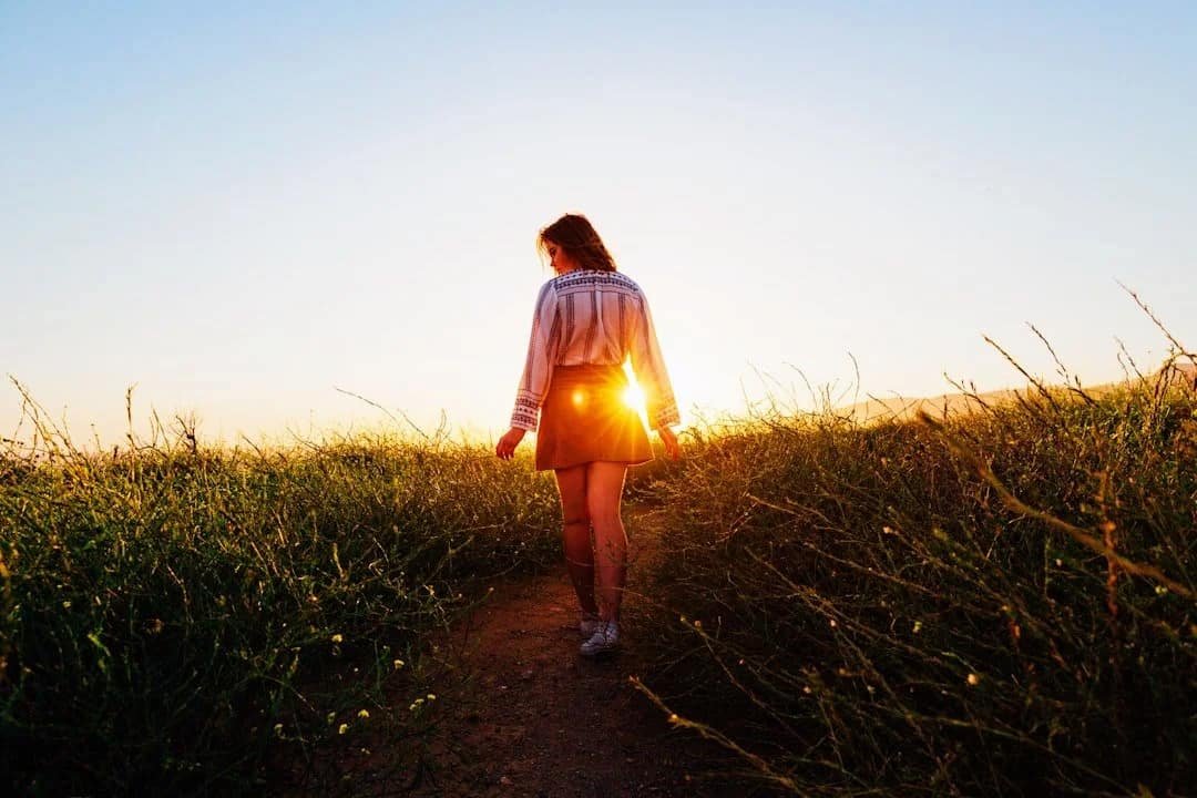 Young adult walking alone on a path through a field at sunset, representing self-discovery, life transitions, comparison, and finding your own pace in young adulthood.