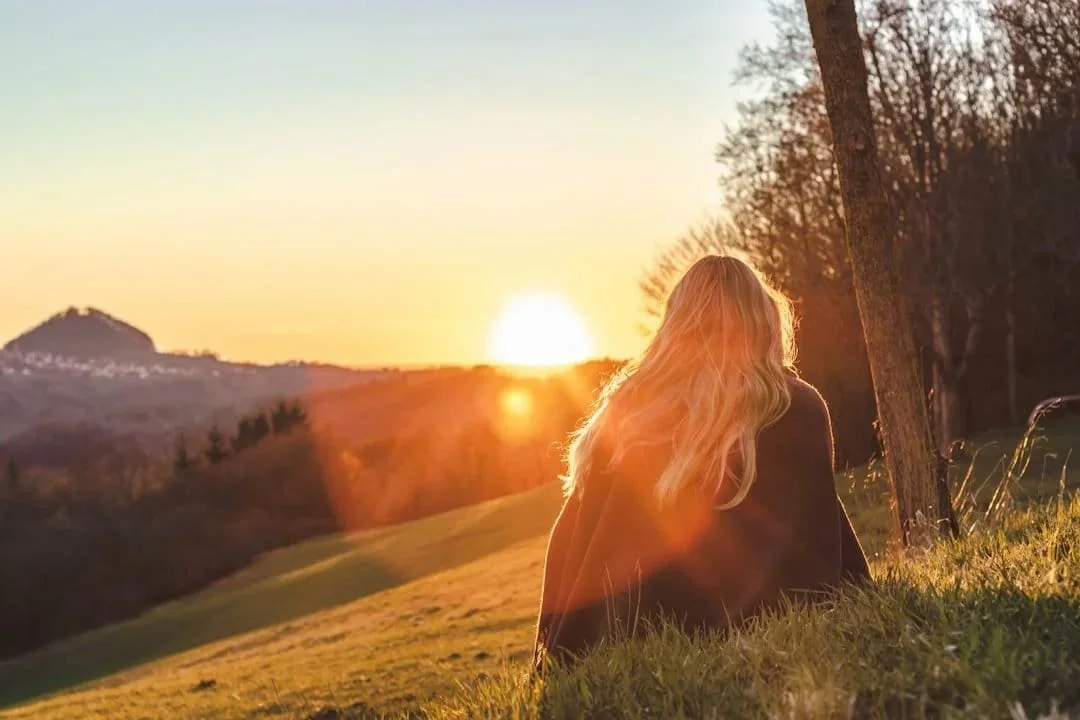 Woman sitting quietly outdoors at sunset, reflecting on healing, personal growth, and creating more choice in how she relates to herself.