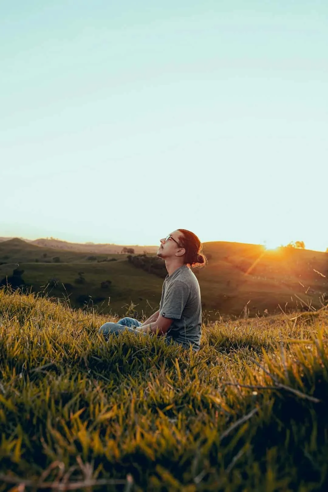 Person sitting quietly in a field at sunset, eyes closed and body relaxed, symbolizing the self-reflection and calm that comes with honoring personal boundaries.