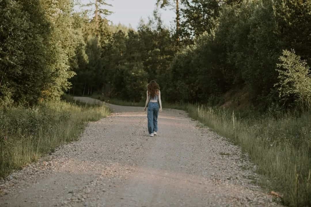 Young woman walking alone down a wooded road, reflecting the uncertainty of navigating life in your 20s.