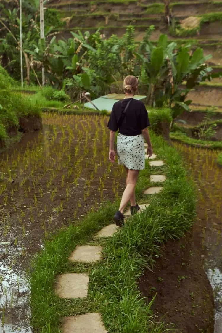 Woman walking along a narrow stepping-stone path surrounded by green fields