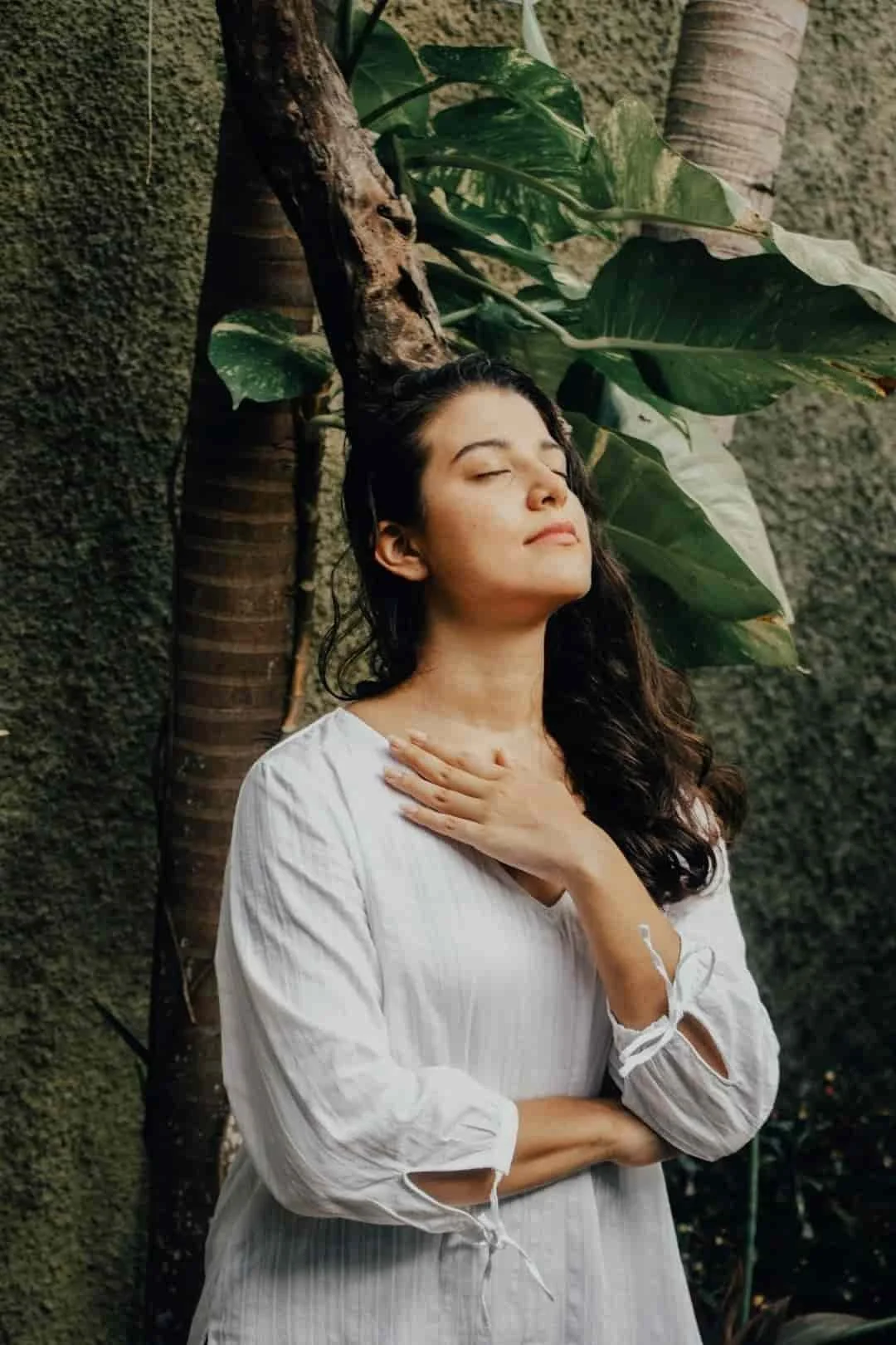 Woman with hand on chest practicing grounded breathing against a moss-covered wall with climbing vines