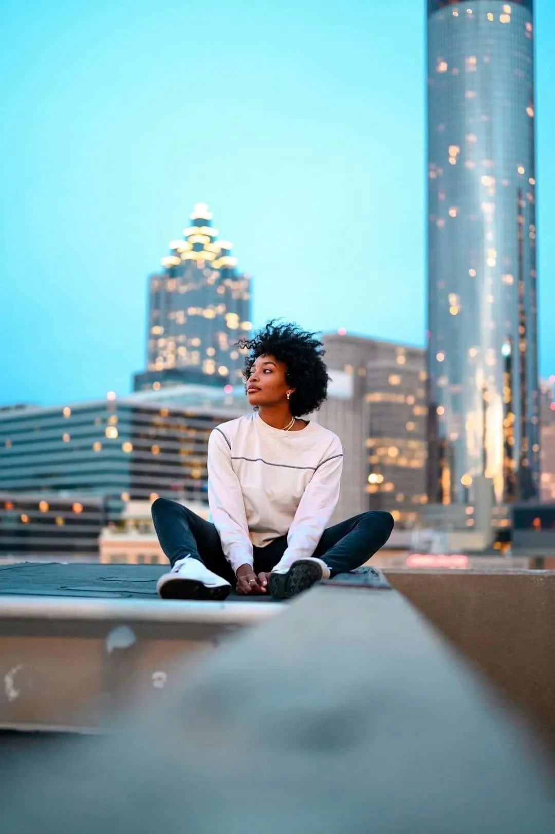 Young adult sitting thoughtfully on a rooftop in a city skyline at dusk, representing identity exploration, life transitions, and finding direction in young adulthood.