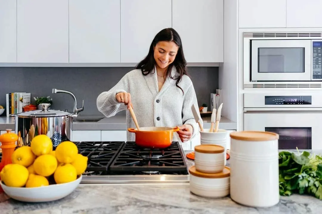 A woman smiling while stirring food in a pot in her kitchen.