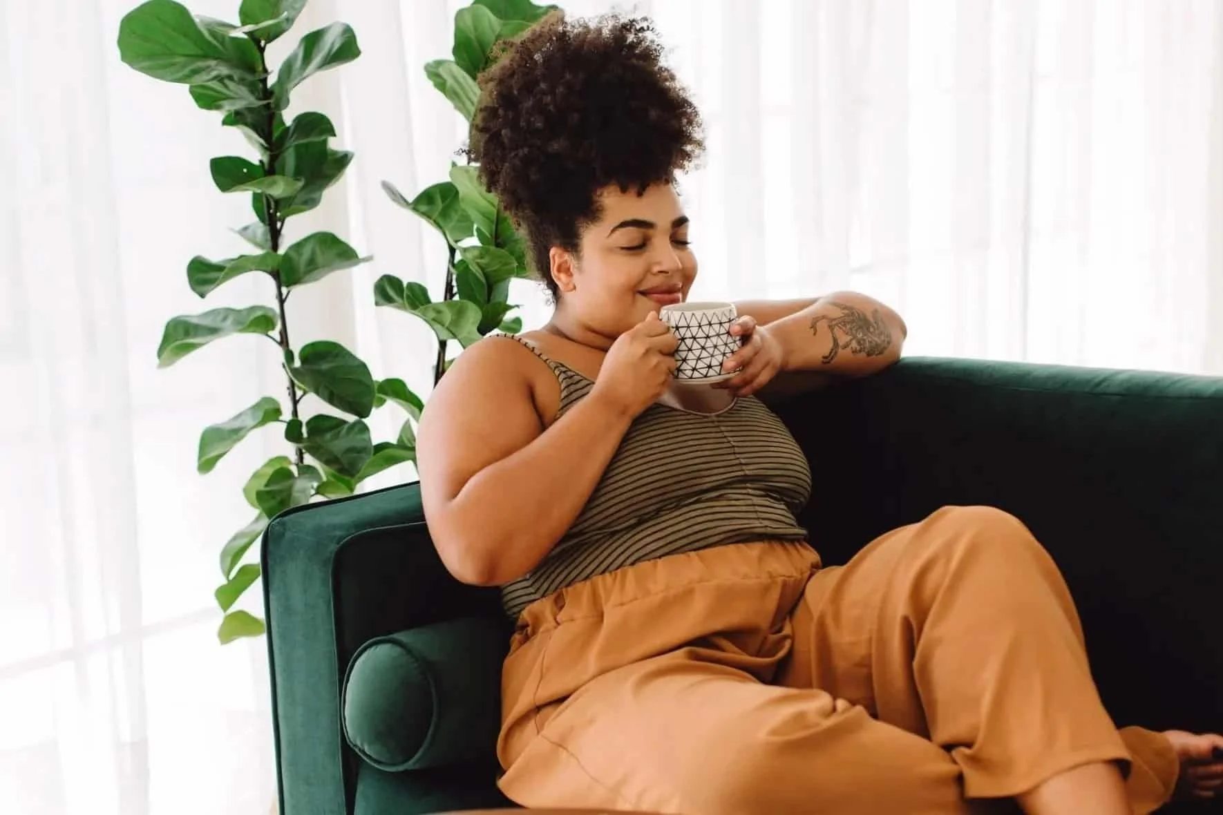 Woman relaxing on a couch with tea in a peaceful home setting, representing the comfort and ease of online therapy.