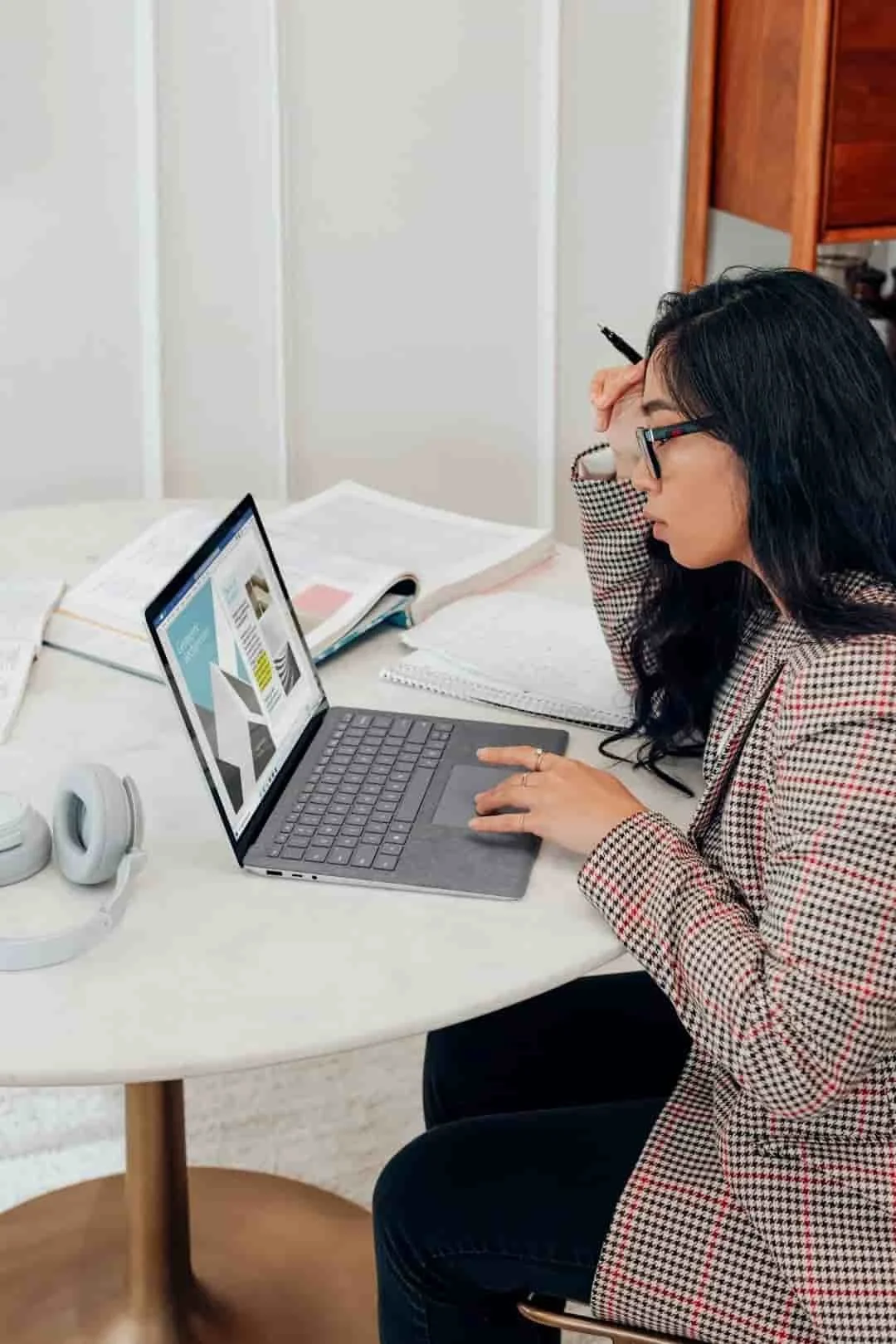 A woman working at a desk on a laptop, appearing focused while seated indoors.