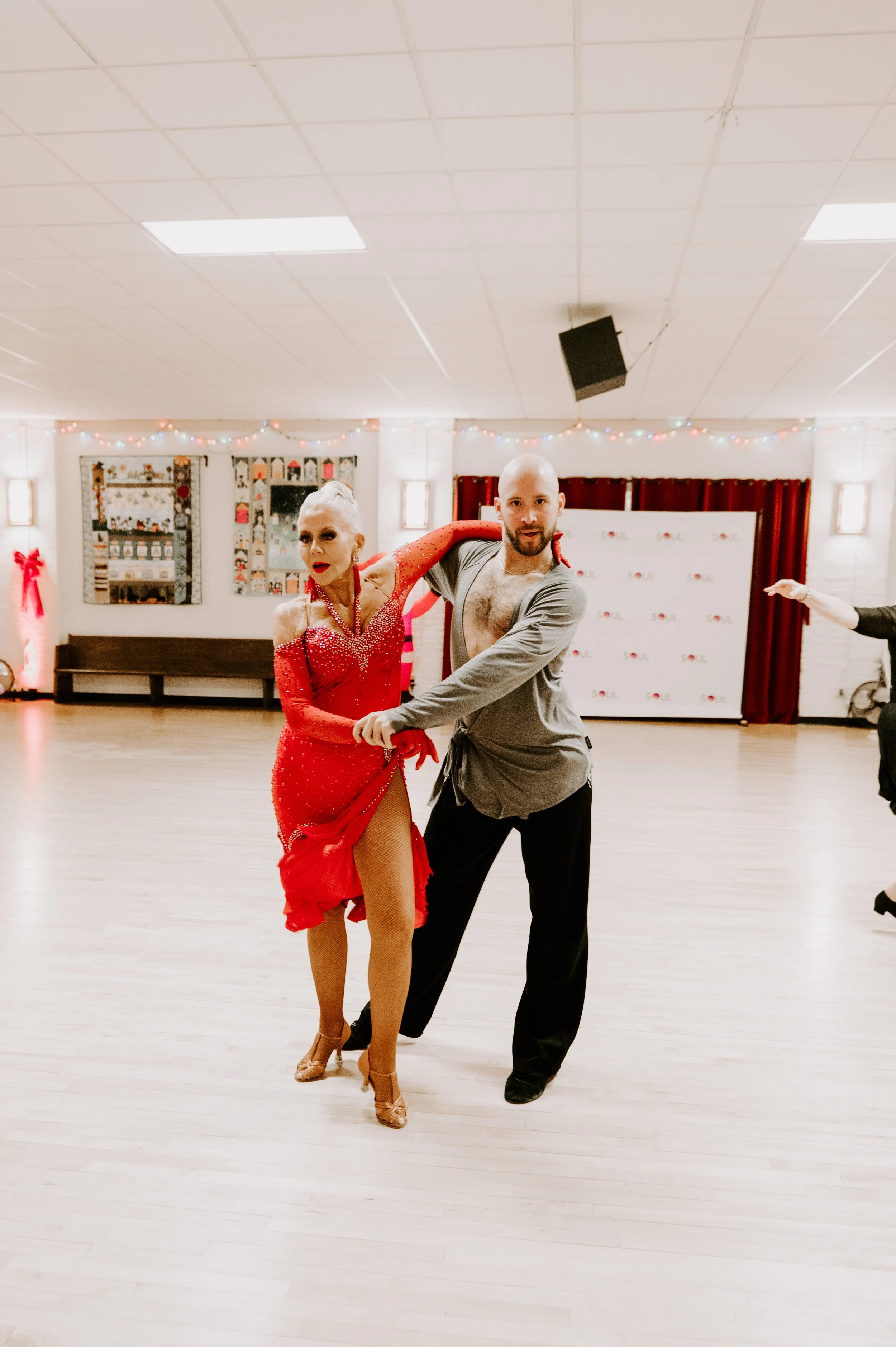 A man and woman dance together on a dance floor with holiday decorations in the background.