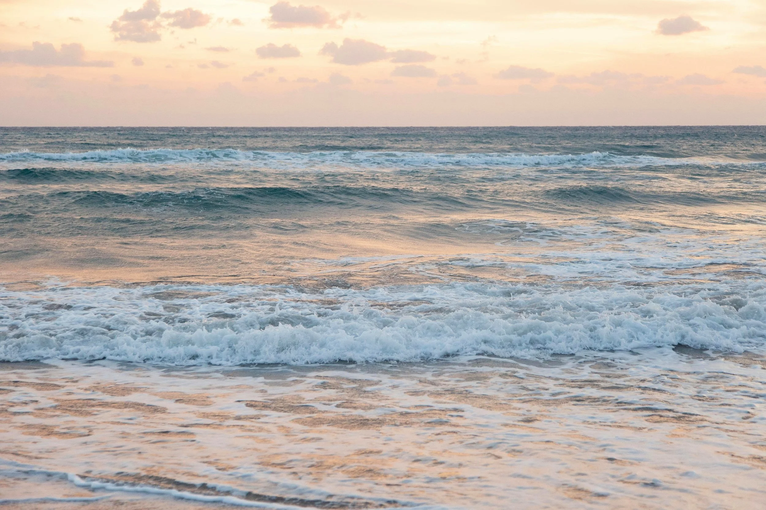 Ocean waves at sunset with a cloudy sky and gentle waves lapping the shore.