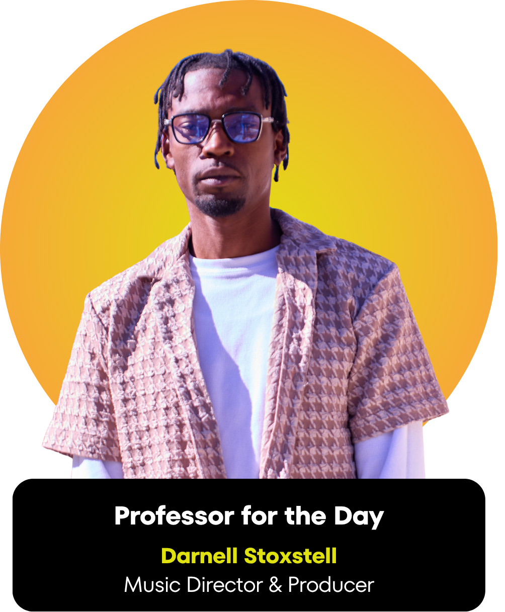 A man with single braids and glasses wearing a patterned shirt over a white T-shirt, standing against a yellow background with an abstract design.