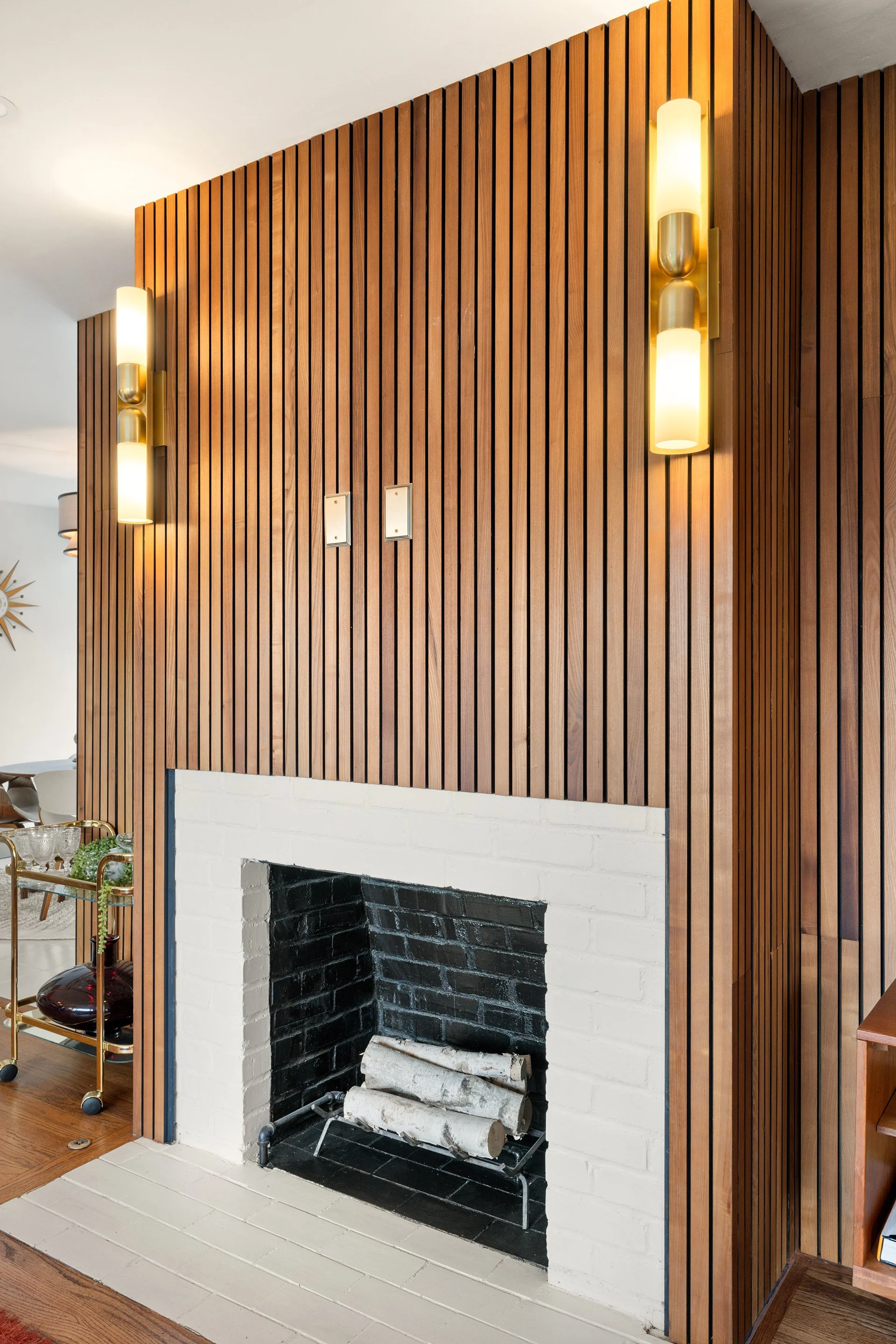 Mid-century modern interior featuring a white brick fireplace with wood paneling and modern sconces.