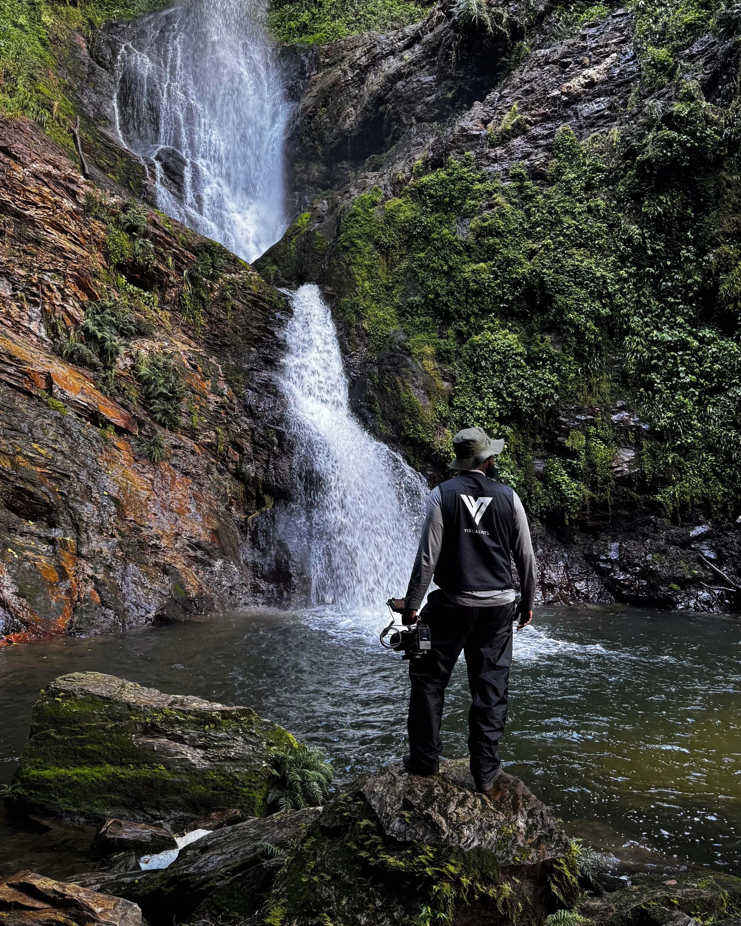 James Rooney looking at the waterfalls, wearing a media vest with Visualists logo in the back