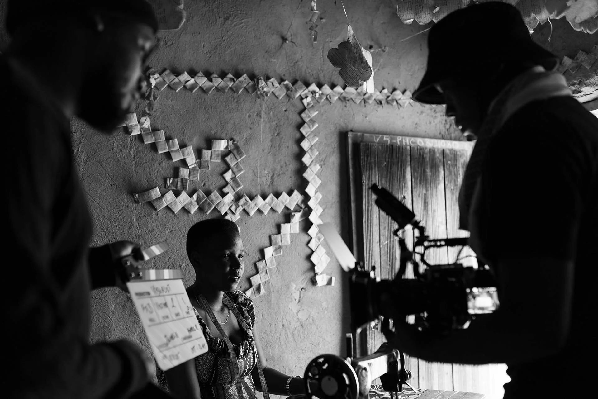 A woman being filmed or photographed in a studio or classroom with paper chain decorations on the wall behind her.
