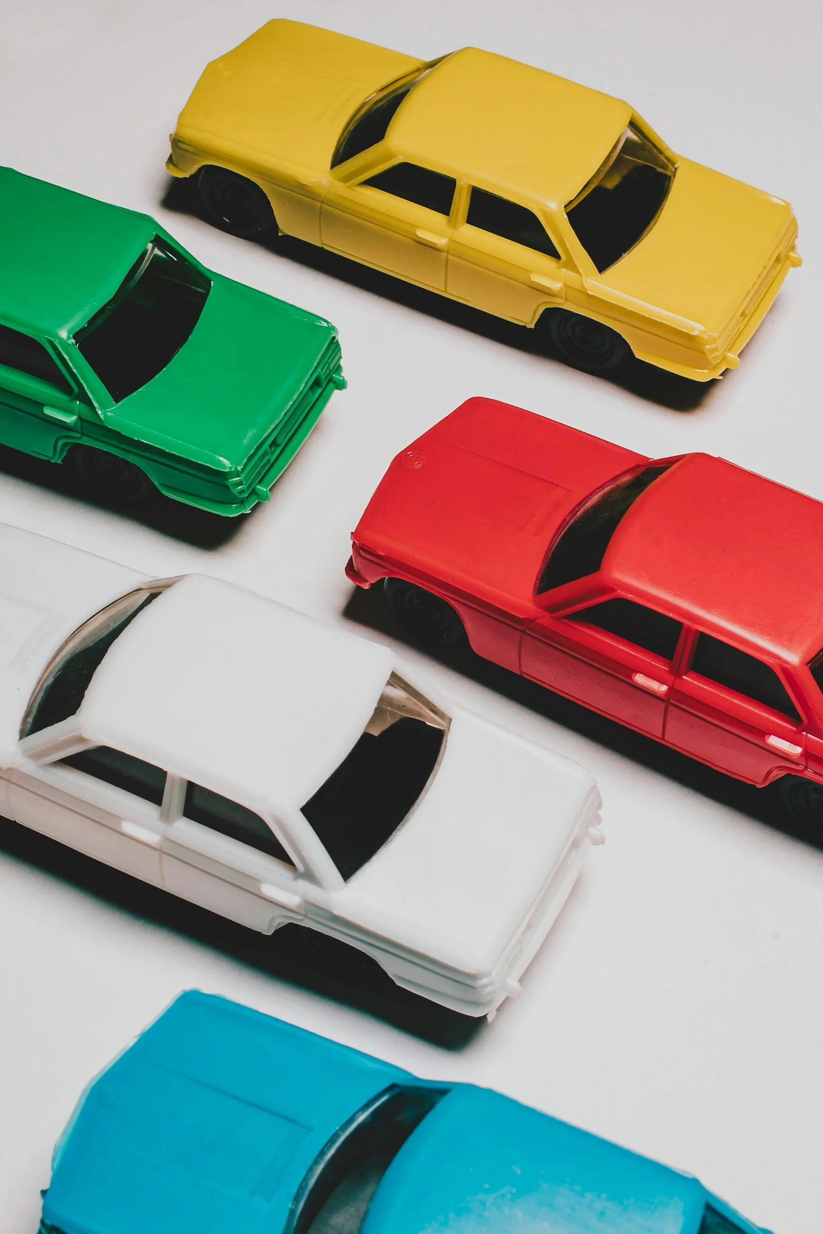Colorful toy cars arranged on a white surface, including green, yellow, red, white, and blue cars.
