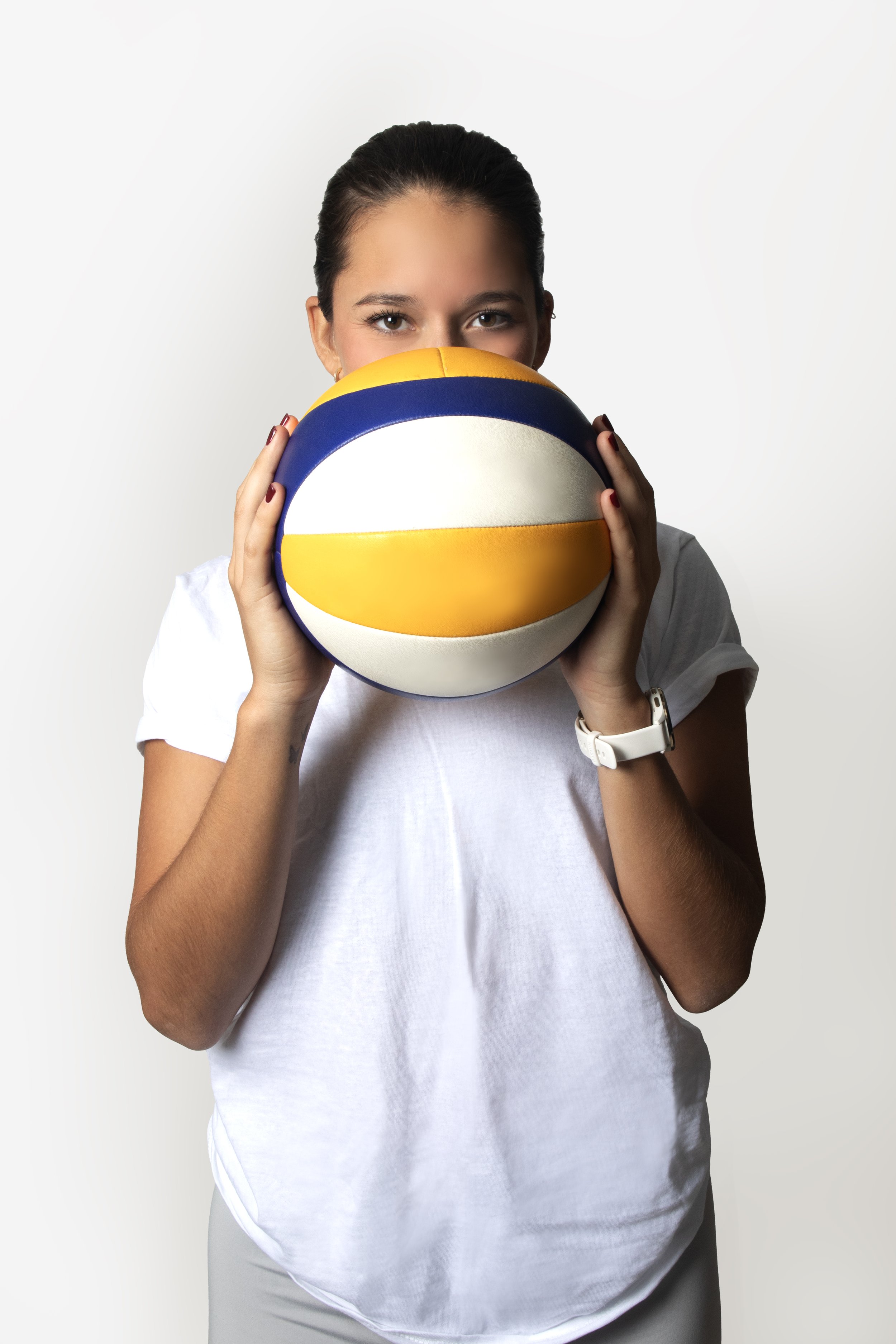 Woman holding a volleyball up to her face, wearing a white shirt.