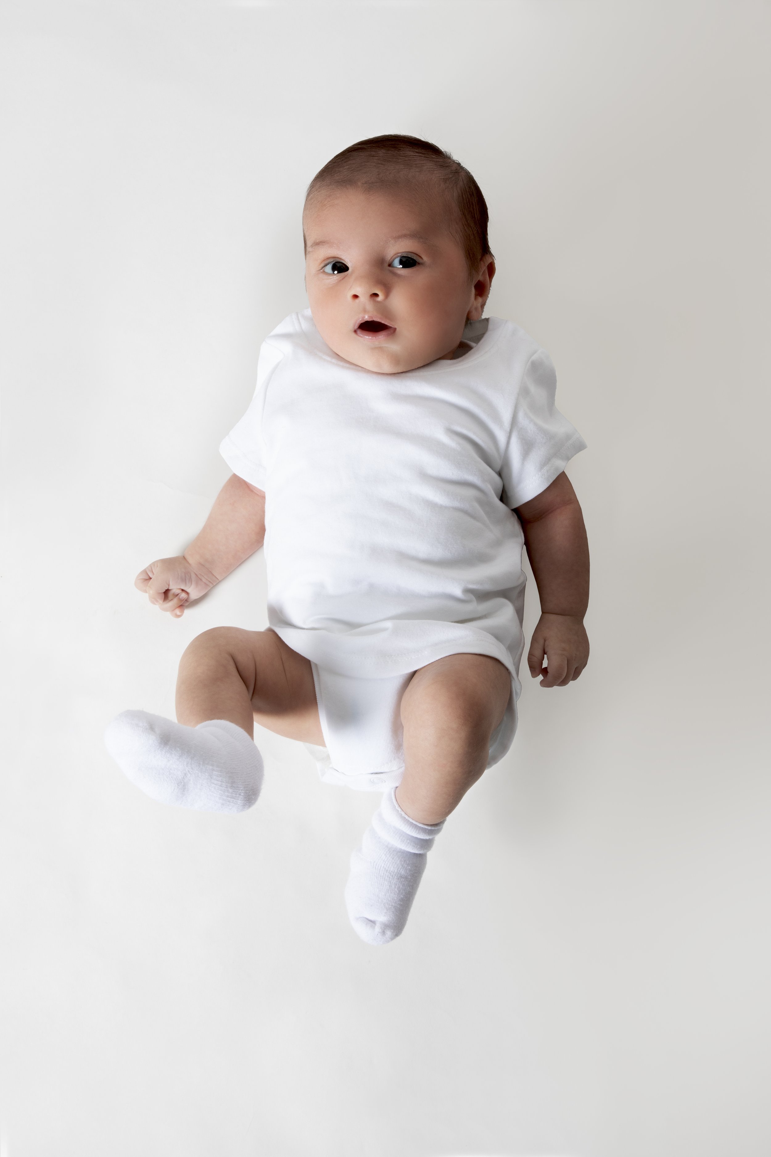 Baby in white onesie lying down on white background.