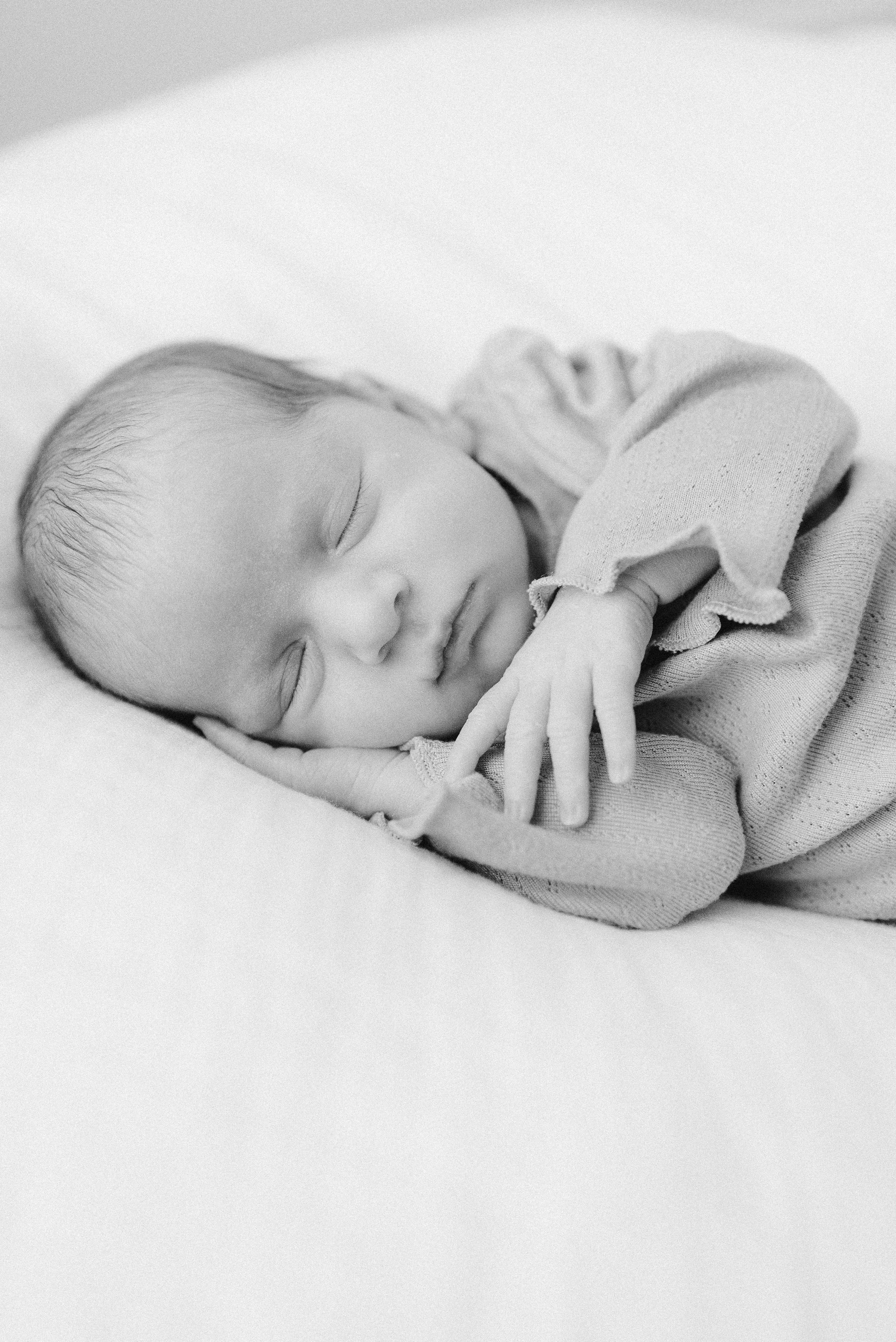 Black and white photograph of a sleeping baby resting on a soft surface, with eyes gently closed and a peaceful expression.