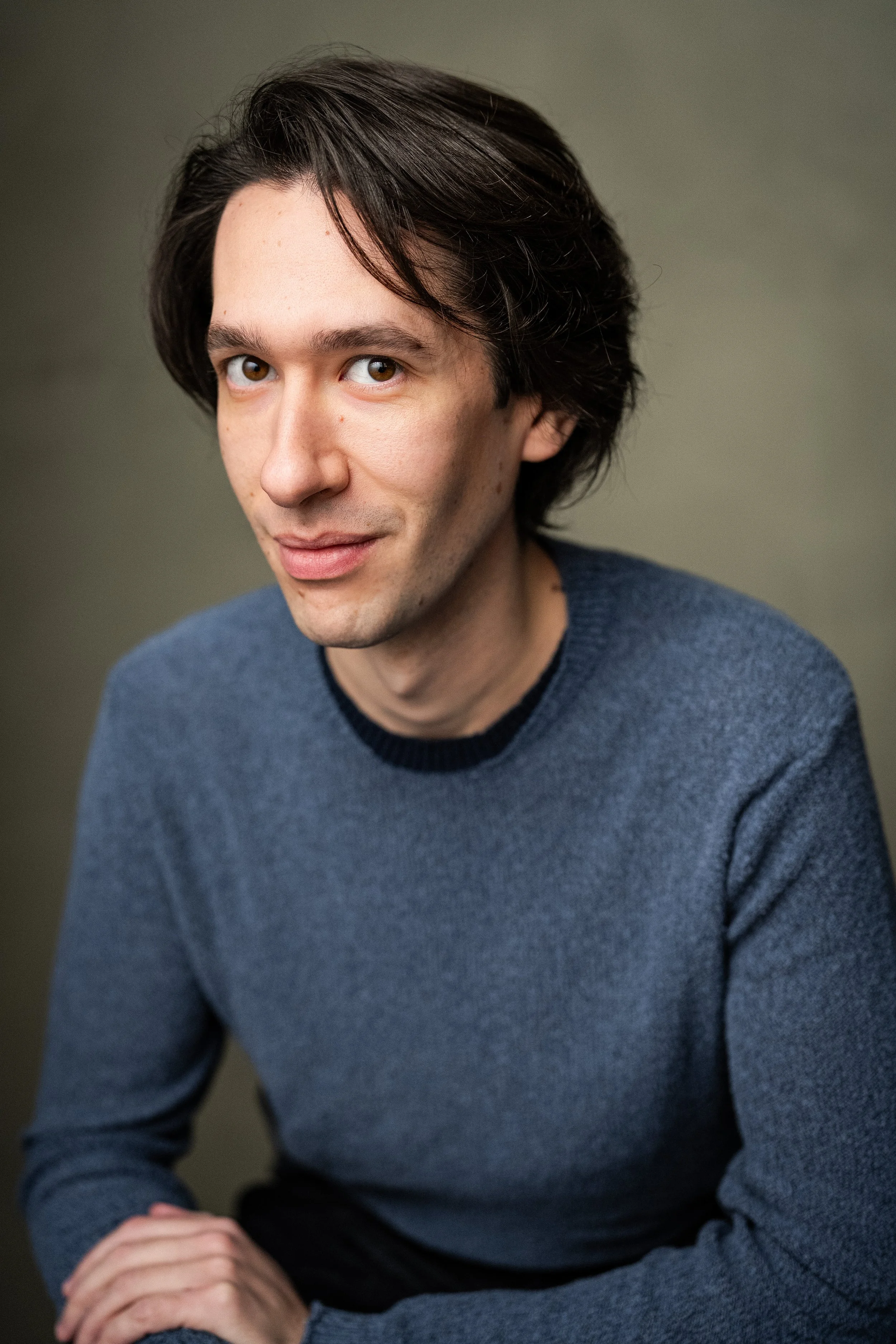 Headshot of actor Christian Pascolutti, smiling, wearing a blue sweater, sitting against a neutral background.