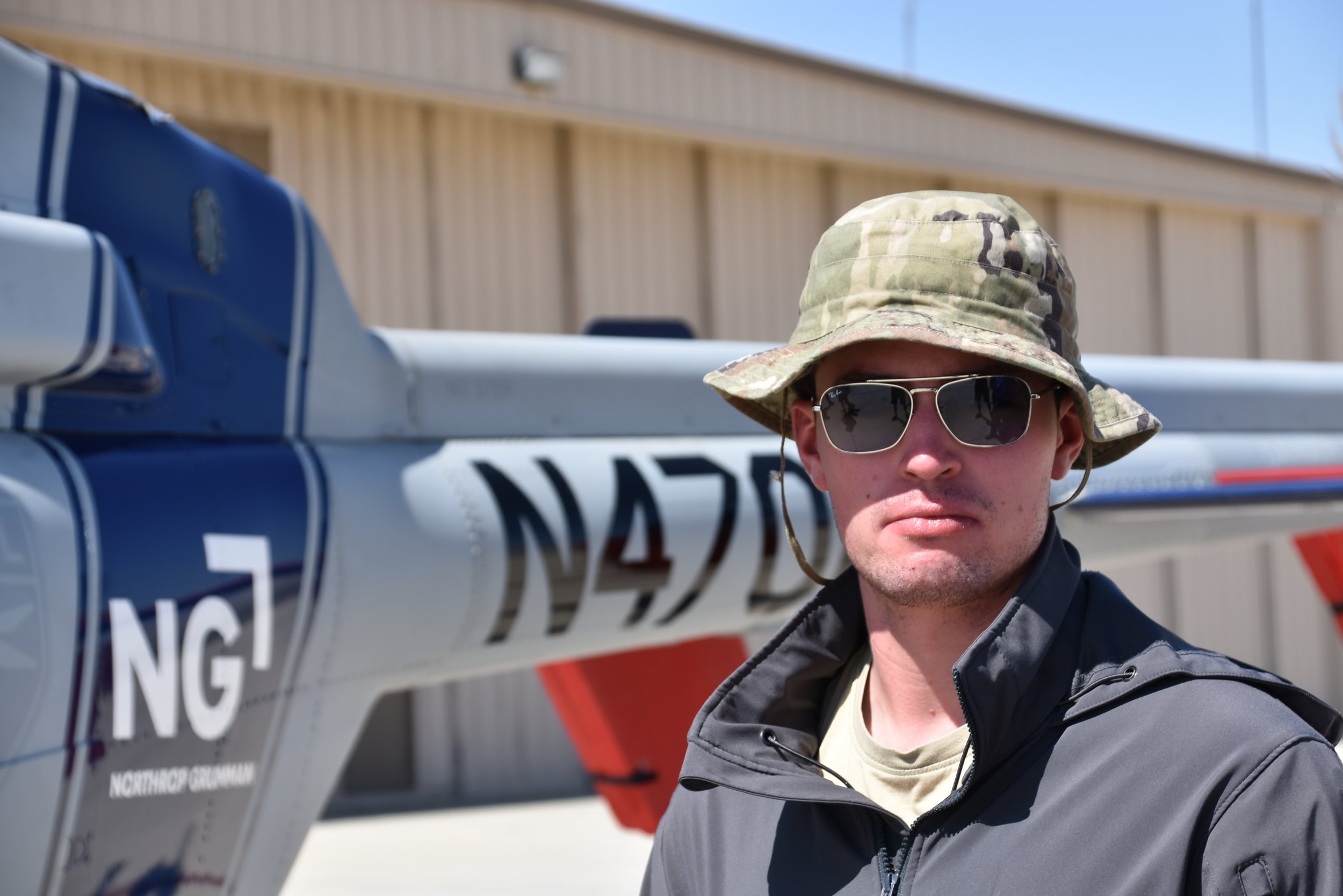 A woman with long, red hair wearing a light blue button-up shirt, smiling against a grey background.