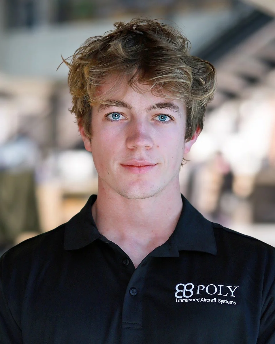 A young man in a suit with glasses, smiling for a professional portrait against a gray background.