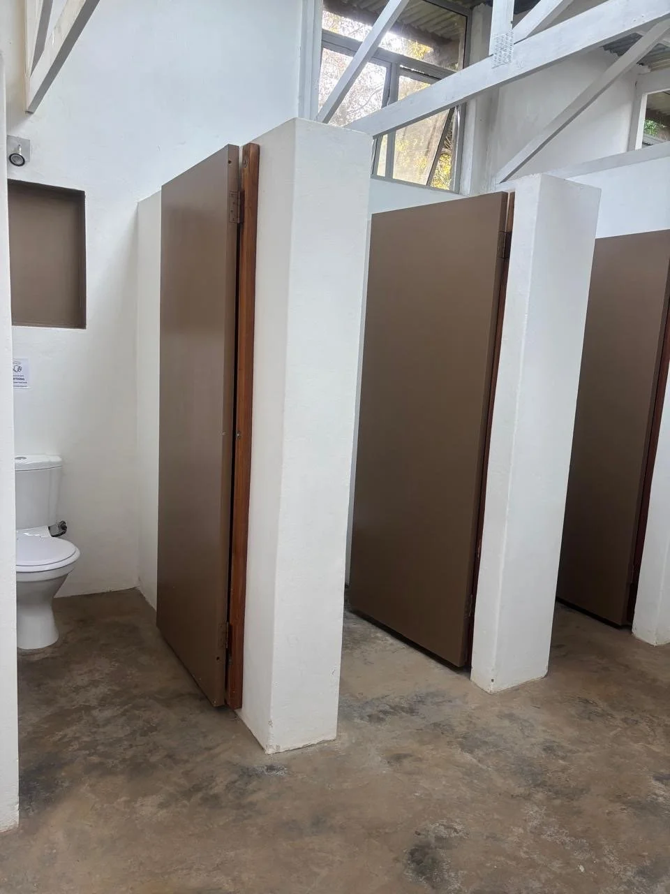 Public restroom with toilet and privacy stalls with brown doors.