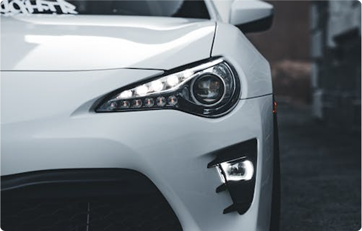 Close-up of the front right side of a white modern car, showing the headlight and fog light.