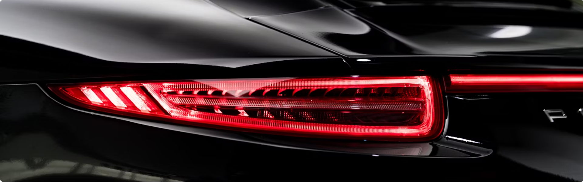 Close-up of the rear light of a black luxury car, showing illuminated red tail lights and sleek curves.