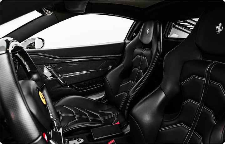 Interior of a luxury sports car with black leather racing seats, a sleek dashboard, and visible Ferrari logo on the steering wheel.