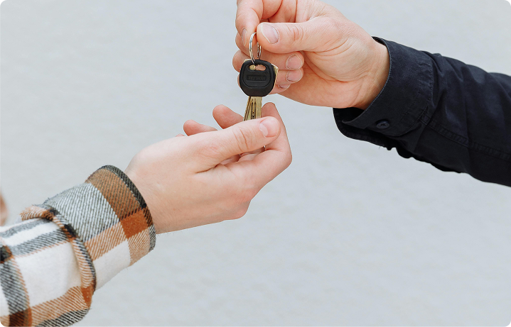 Two people exchanging a car key with one person handing it over and the other holding it.
