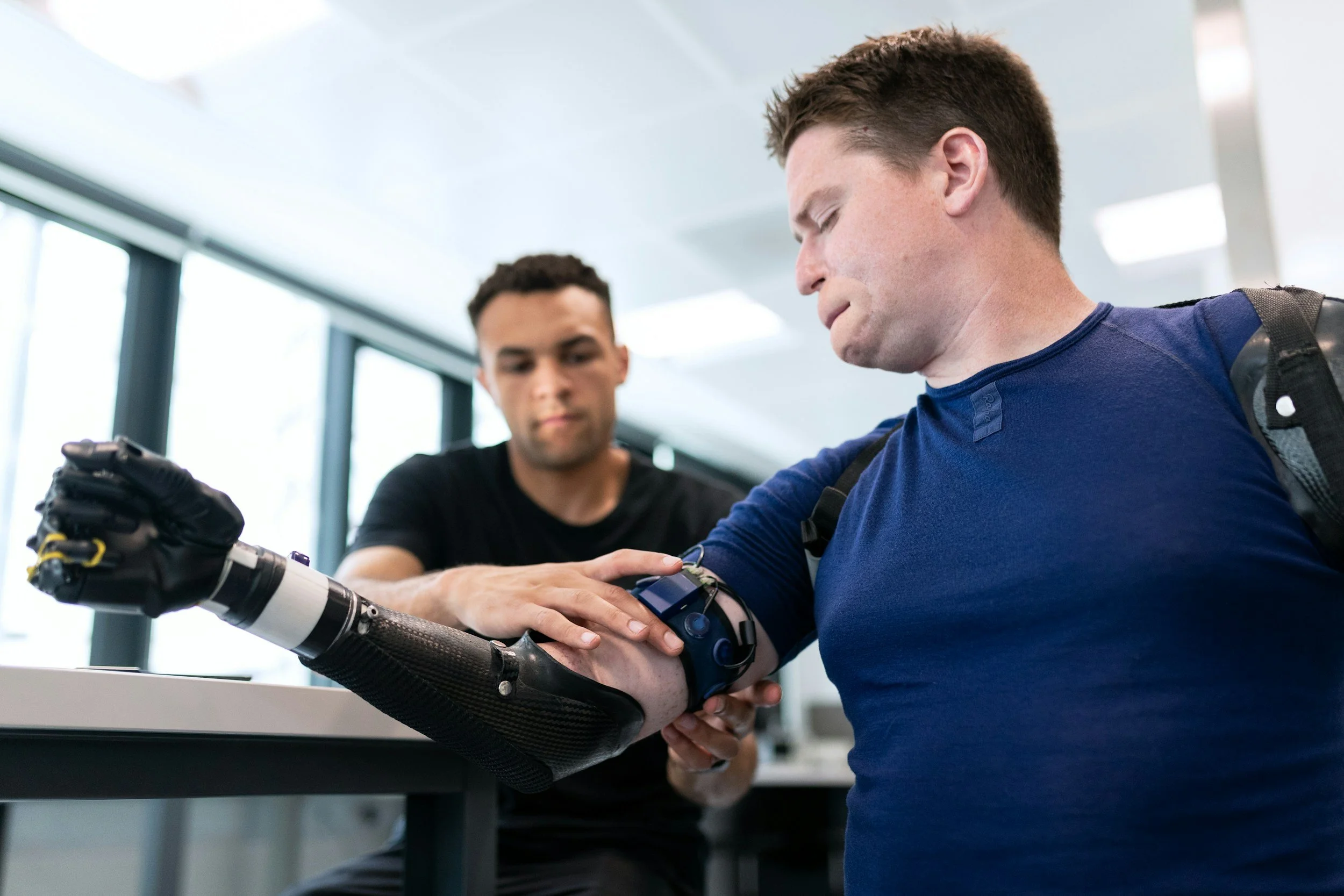 A man with a prosthetic arm is being fitted with a medical device by a professional in a clinical setting.
