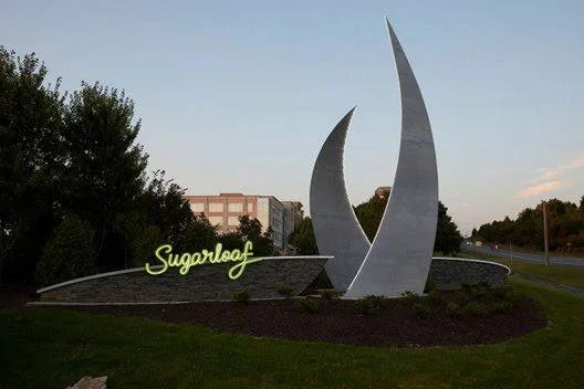 The Sugarloaf monument with three tall, curved structures and the word "Sugarloaf" in yellow neon sign on a landscaped area.