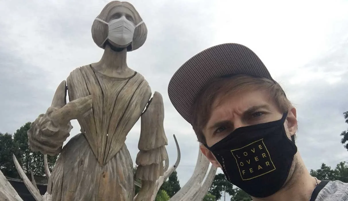 Man wearing a mask standing in front of a statue with a mask.