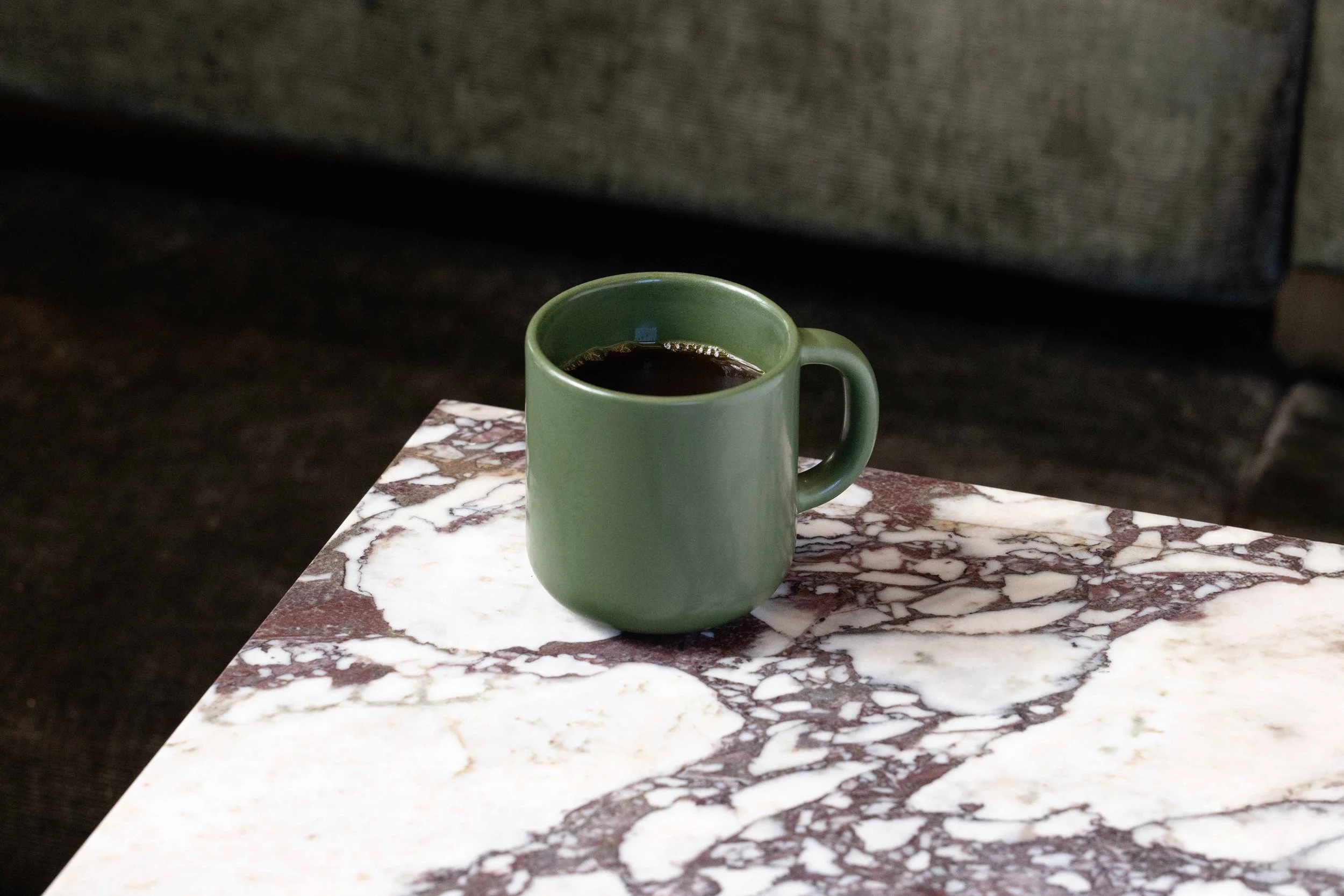 A green mug of coffee on a white and red marble table