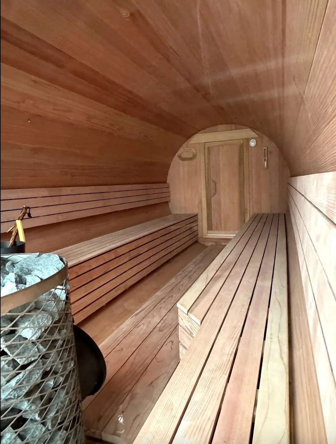 Interior of a wooden sauna with benches along both sides and a heater with rocks in the corner.