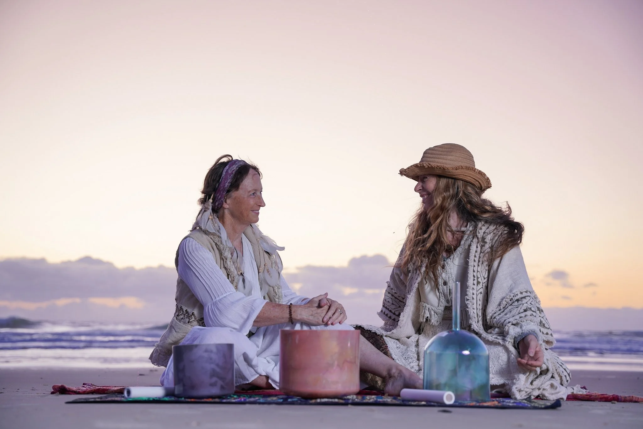 Annie & Anita sound practitioners sitting on the beach with instruments