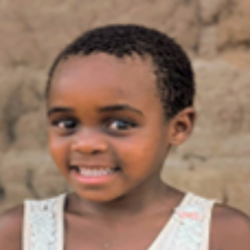 Portrait of a young girl smiling outdoors in front of a light-colored stone wall.