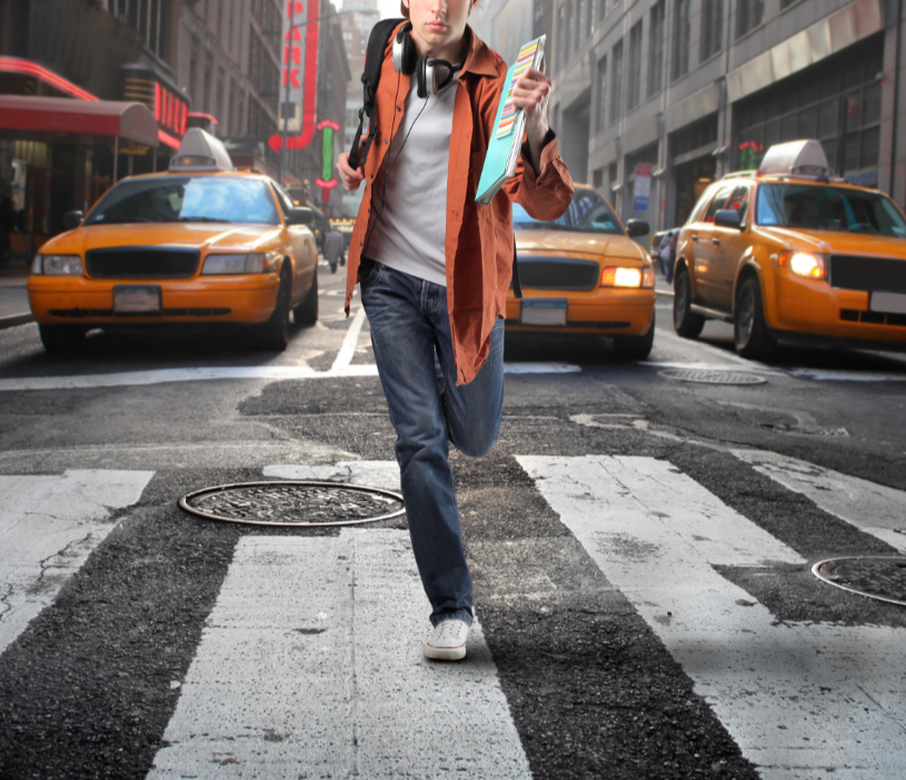 Person running across a city street with yellow taxis and tall buildings in the background