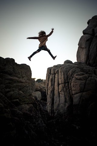 Person jumping between rocky cliffs at sunset or sunrise.