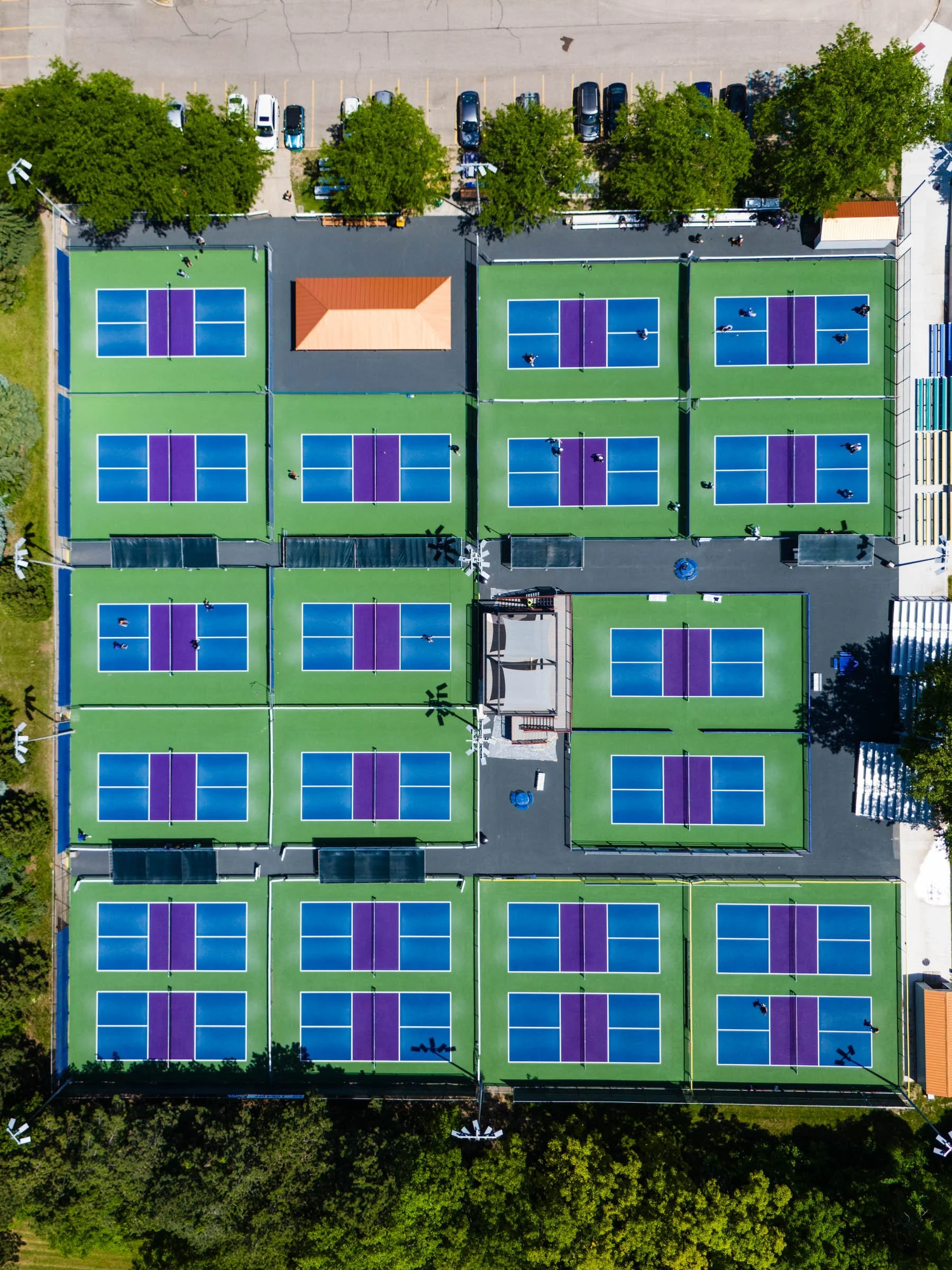 Aerial view of Belknap Park Pickleball Courts, Home of the Beer City Open, featuring twenty one pickleball courts with blue and purple surfaces, surrounded by green trees and parking lot.
