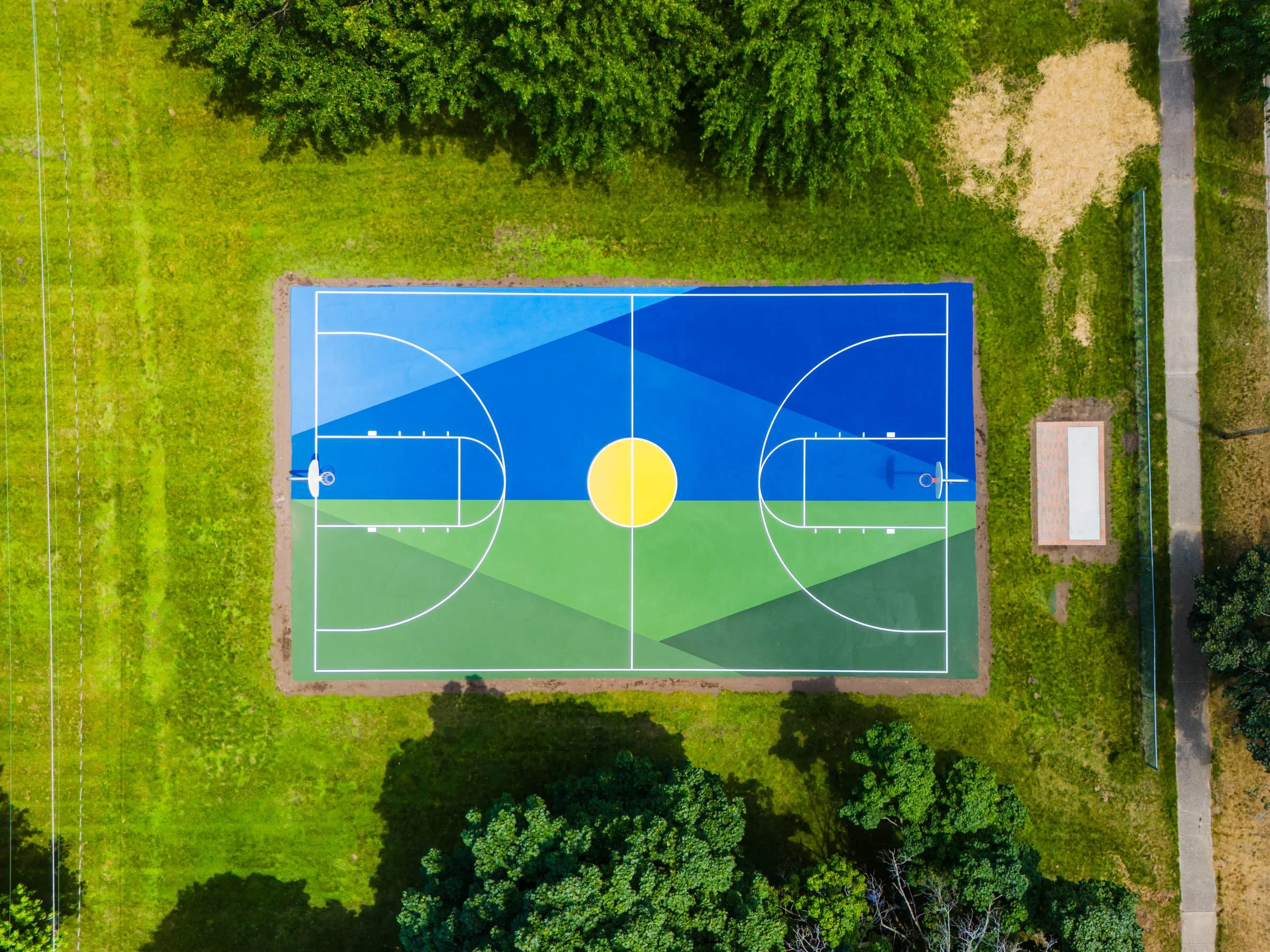 An aerial view of a colorful basketball court, in Grand Haven Michigan surrounded by green grass and trees.