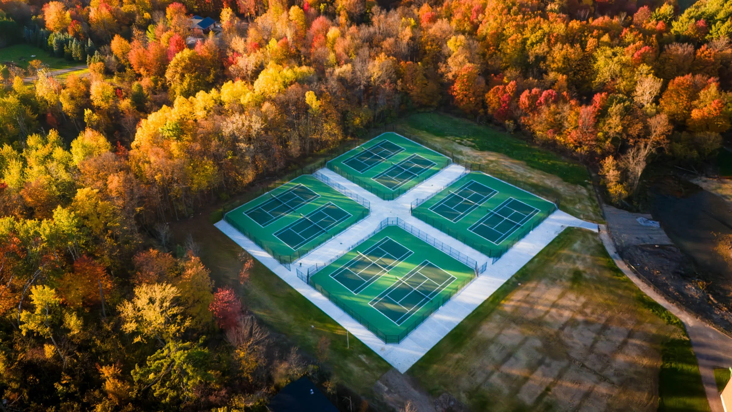 Aerial view of eight post tension concrete tennis courts in Michigan surrounded by trees with fall foliage, situated in a park or recreational area.