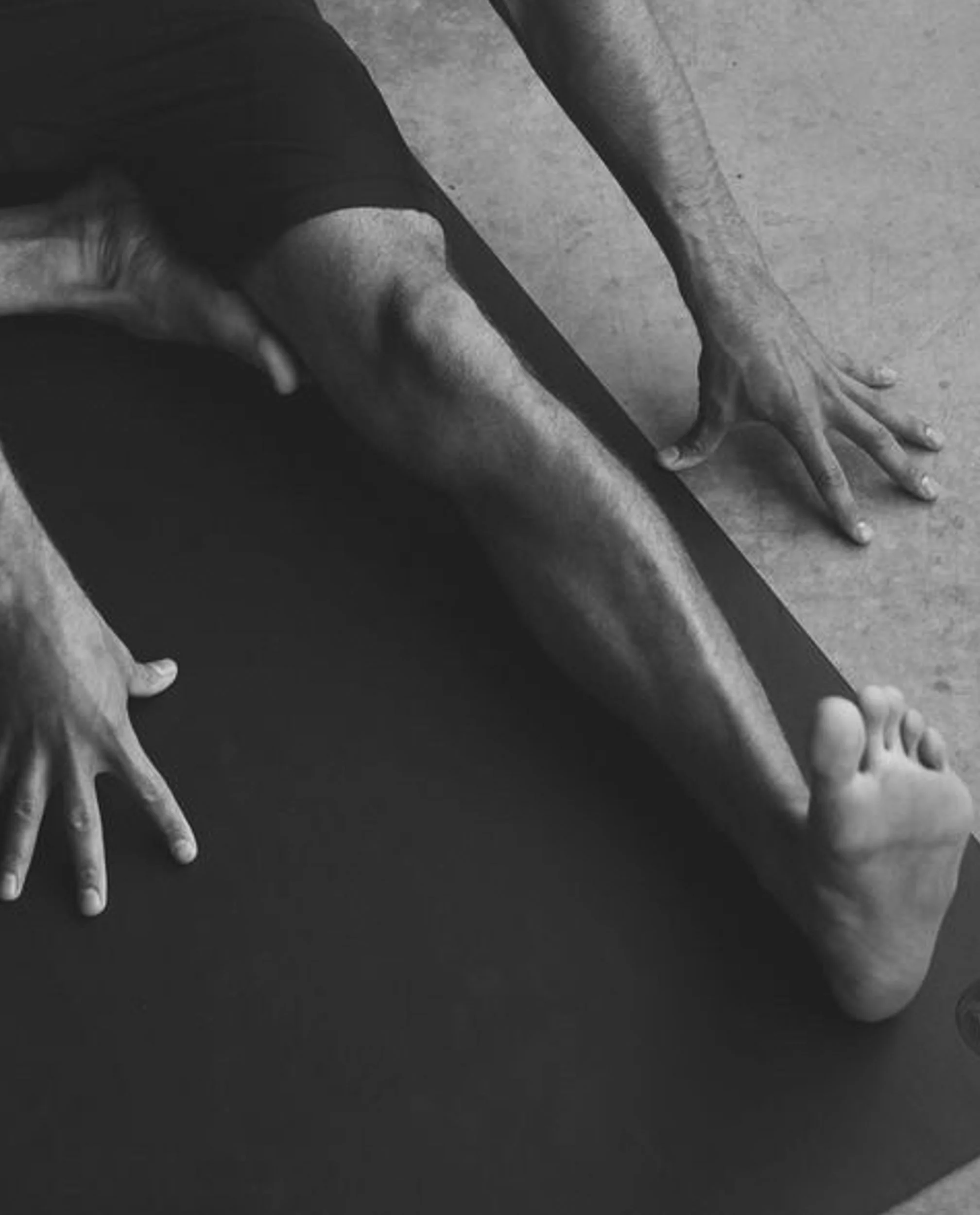 A person performing a yoga or stretching pose on a black mat, with hands and feet on the ground, in black and white.