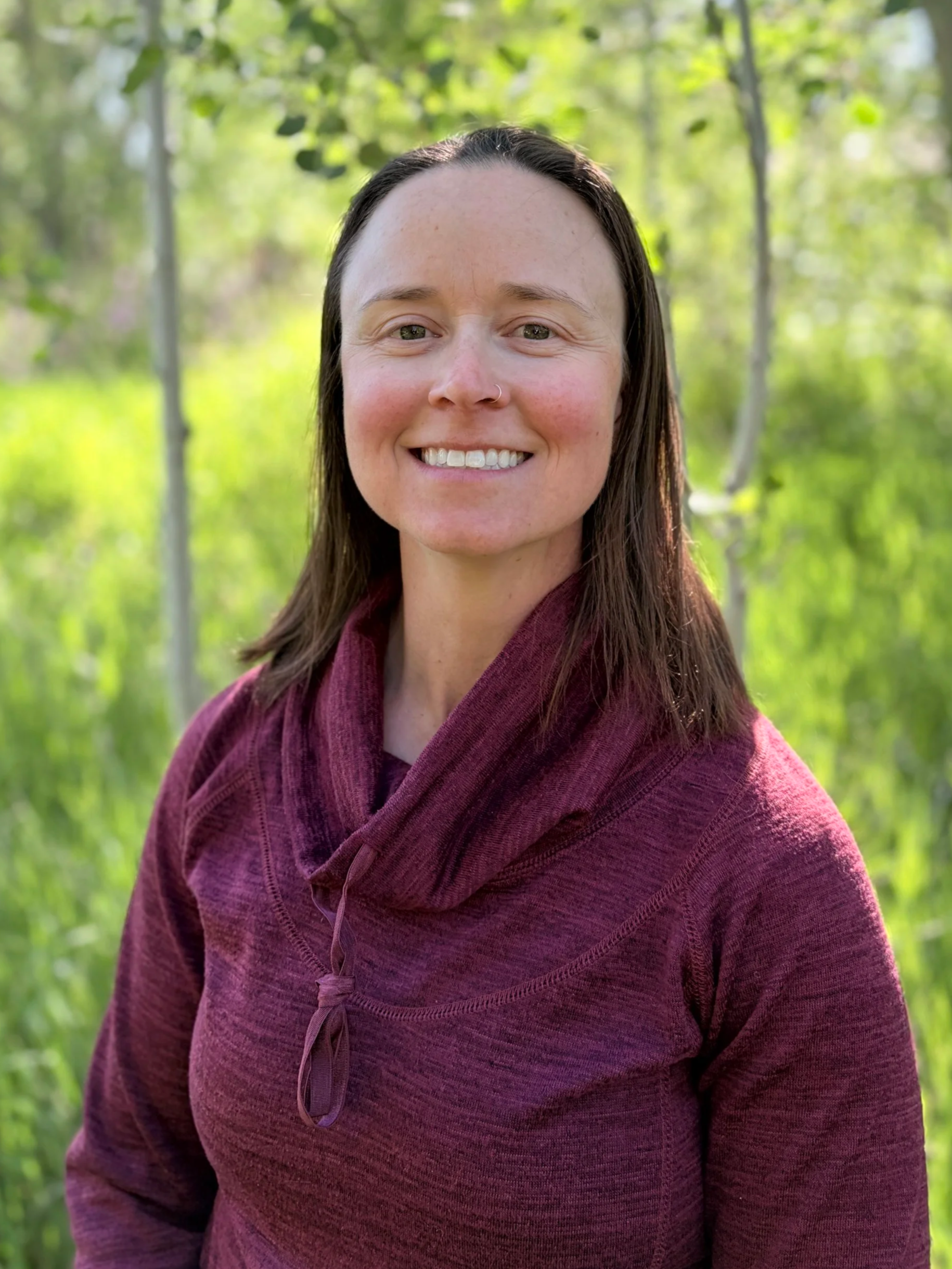 Person smiling outdoors with autumn foliage in the background.